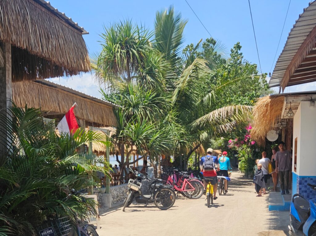 Bicycles parked along the sandy beach road in the north of Gili Air, lined with restaurants, palm trees and an Indonesian flag