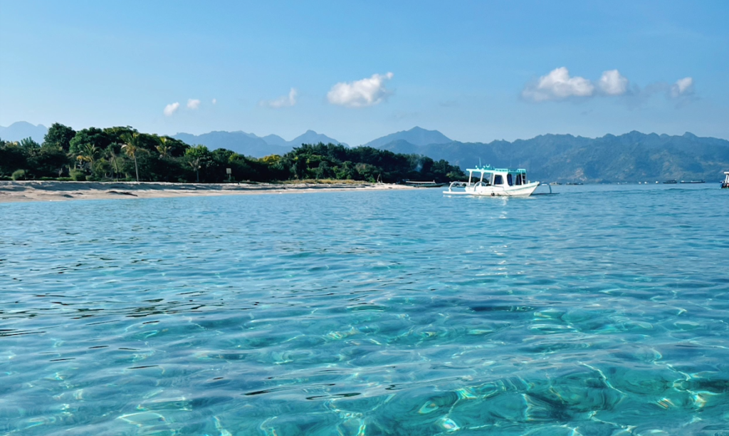 Crystal clear turquoise water at Gili Air, with a traditional boat and Lombok mountains in the background