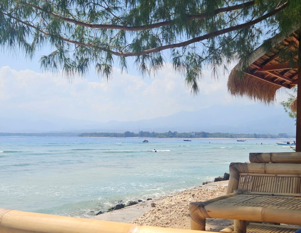 Bamboo seats under shady trees on a quiet beach on Gili Air, with turquoise water and a view across to Lombok