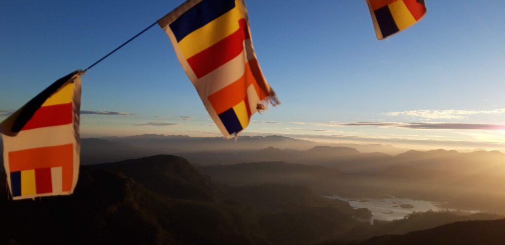 Buddhist flags on Adam’s Peak in Sri Lanka, with a sunrise view over hills and a lake