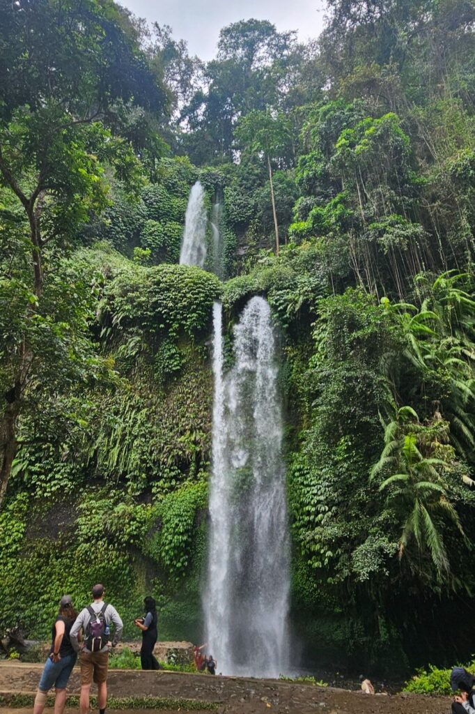 Sendang Gile waterfall in Lombok, falling down a jungle-covered cliff with visitors standing at the base
